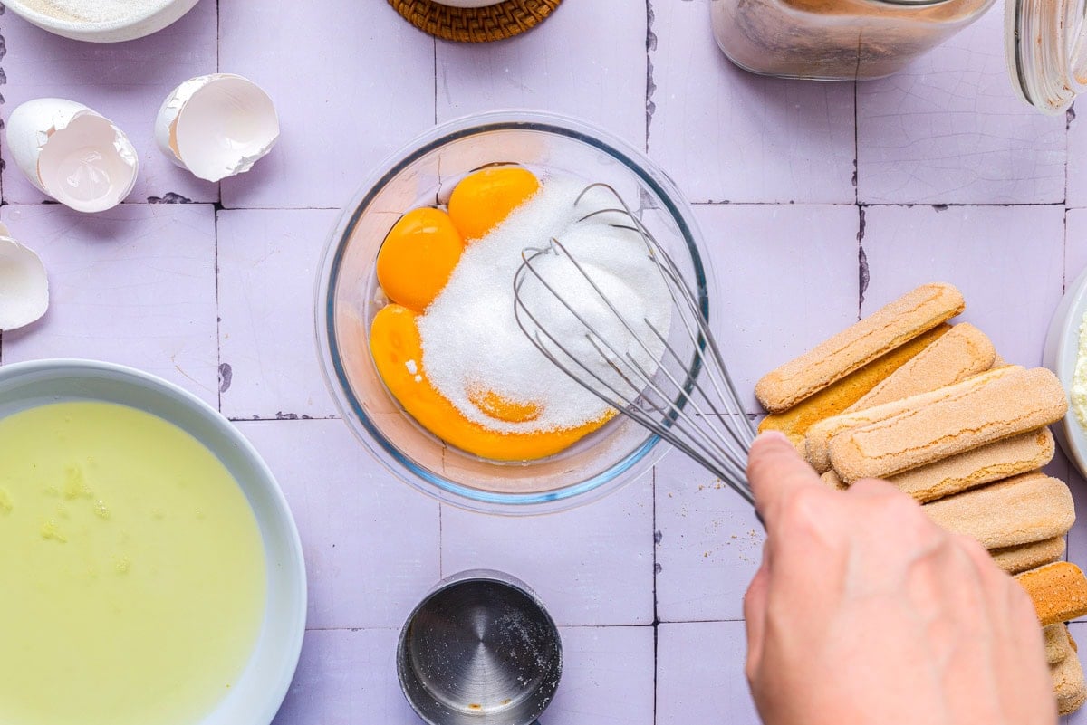 white sugar in glass bowl with egg yolks being whisked.