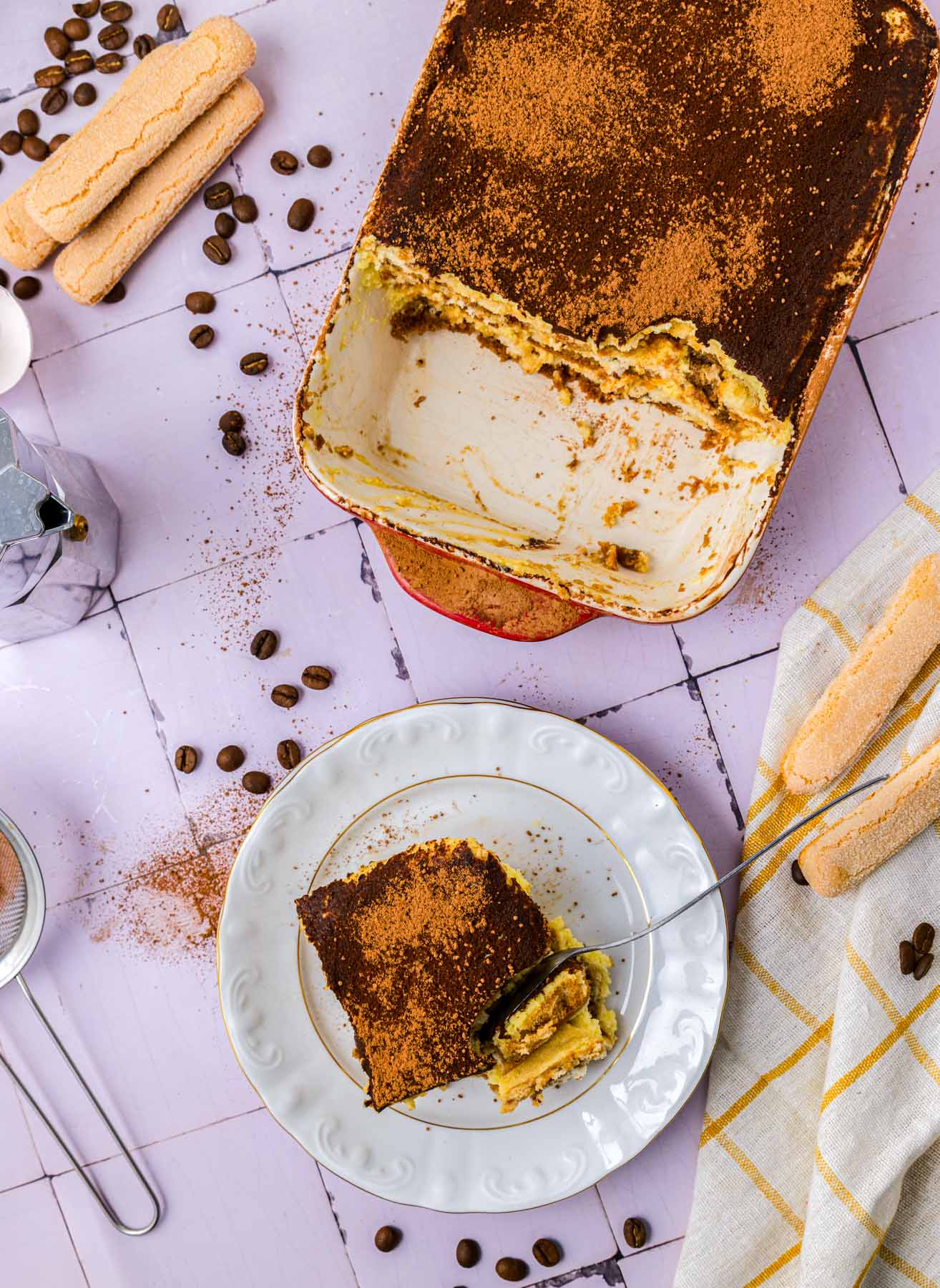 pan of tiramisu with slice removed and sitting on plate on counter.