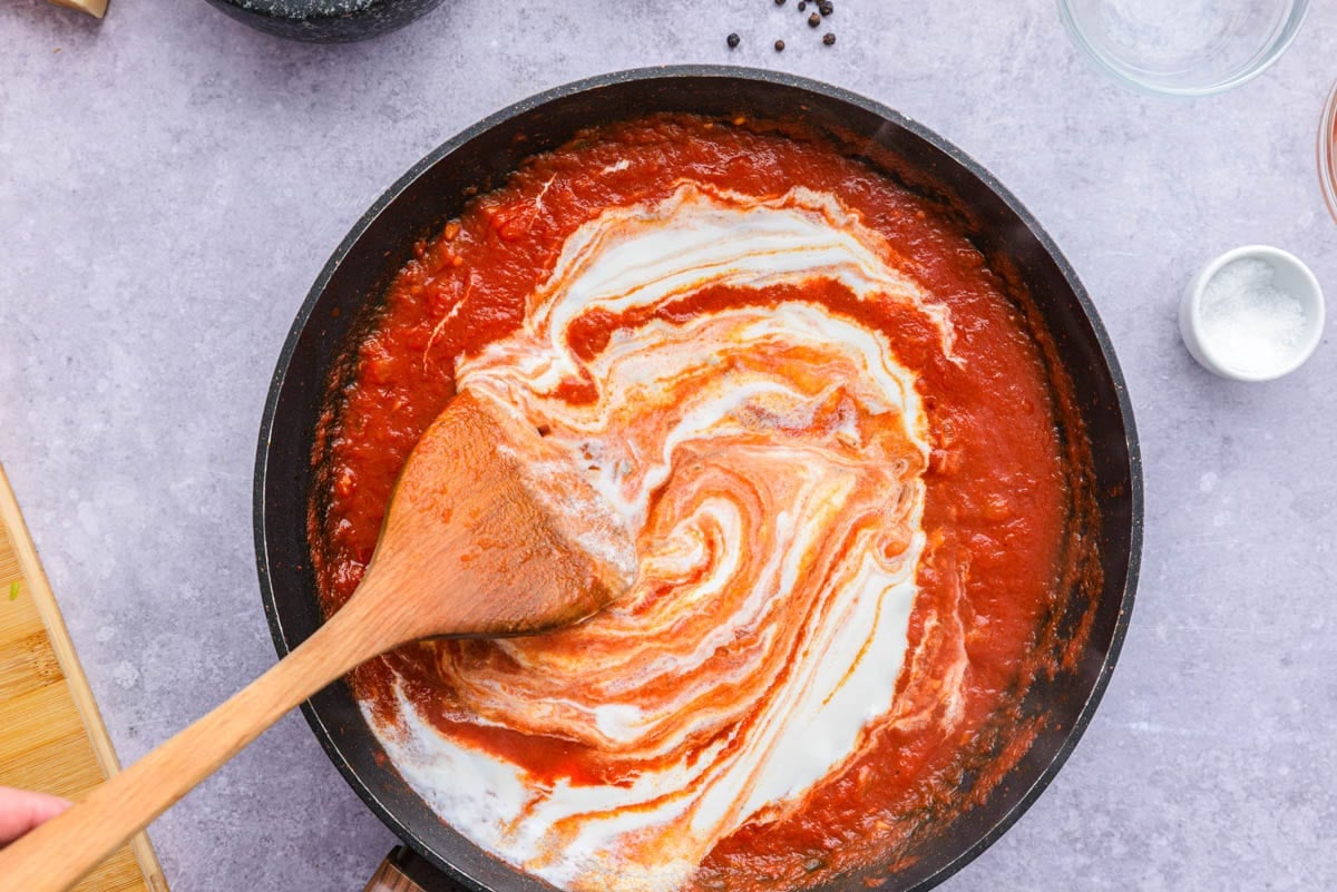 cream stirring into sauce pan of tomato sauce.