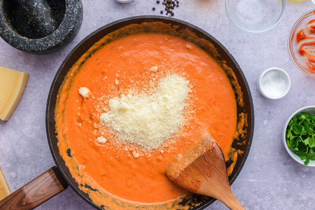 grated parmesan cheese on top of rose sauce in sauce pan.