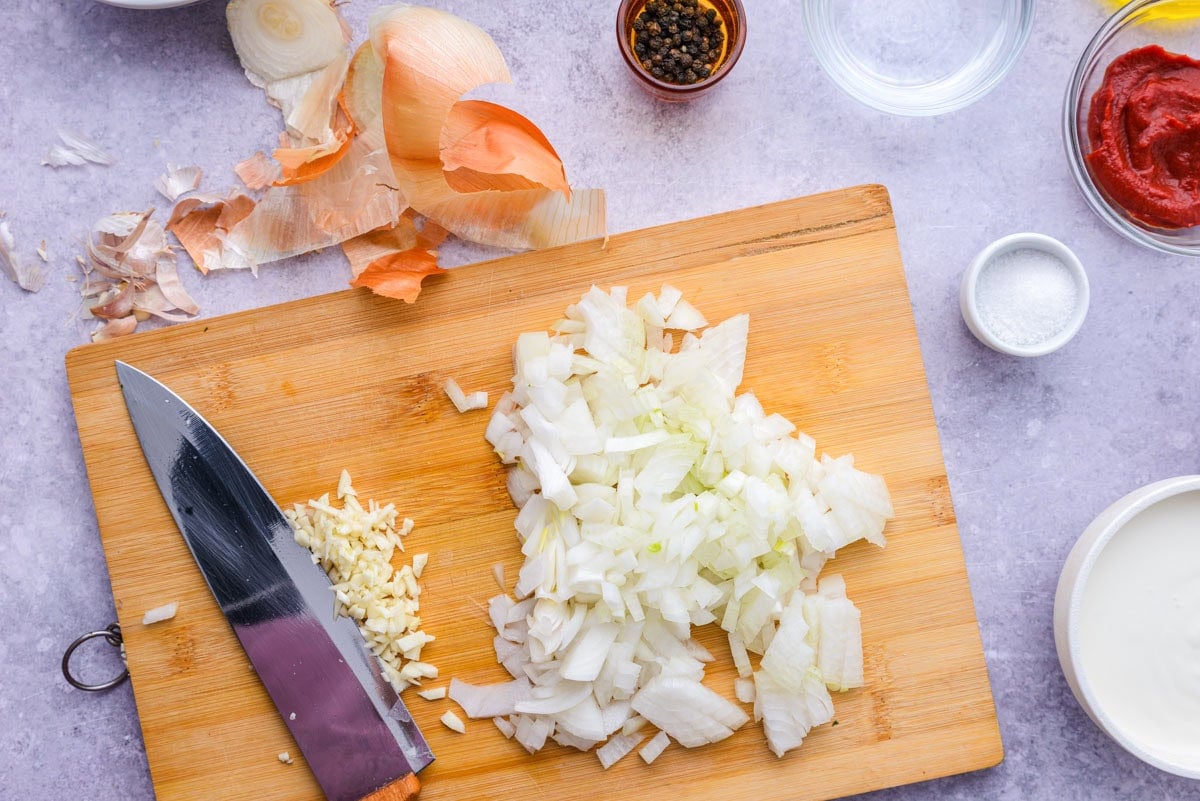 onions and garlic chopped on wooden cutting board on counter.