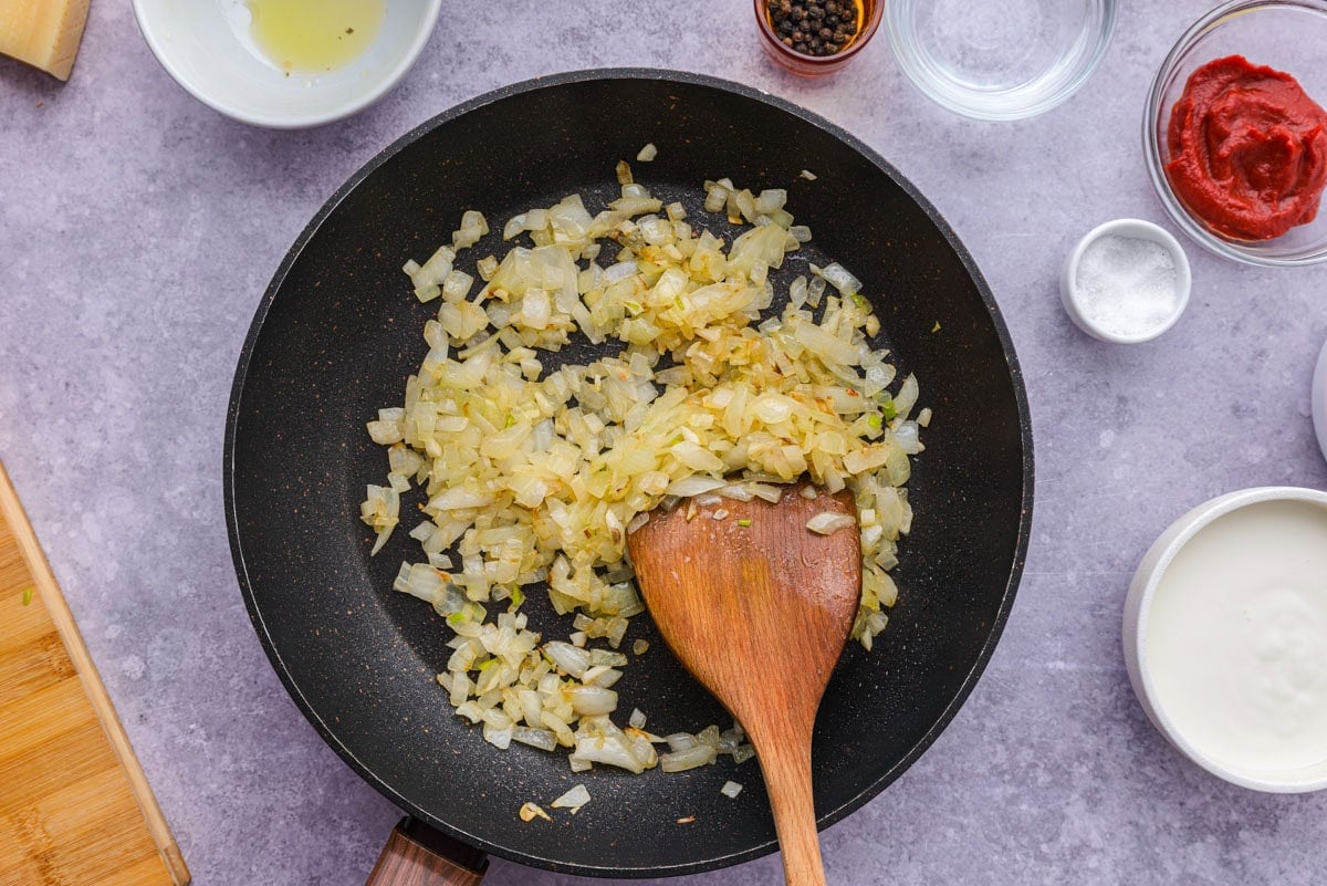 onions browning in frying pan with wooden spoon stirring.