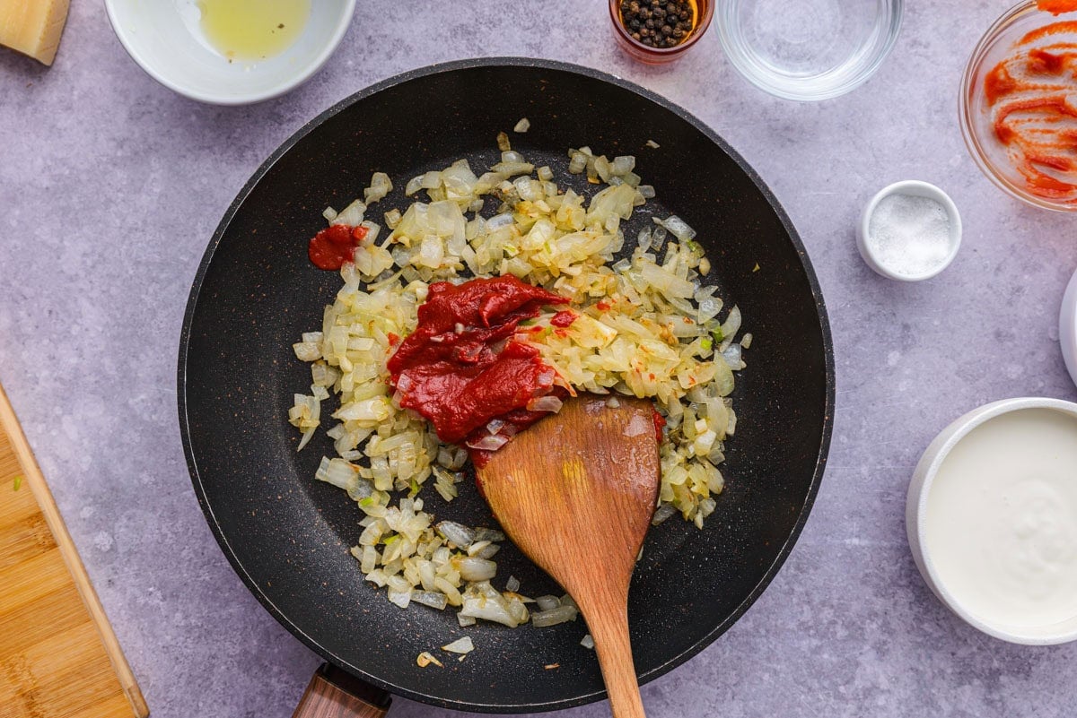tomato paste in frying pan of browned onions with counter around.