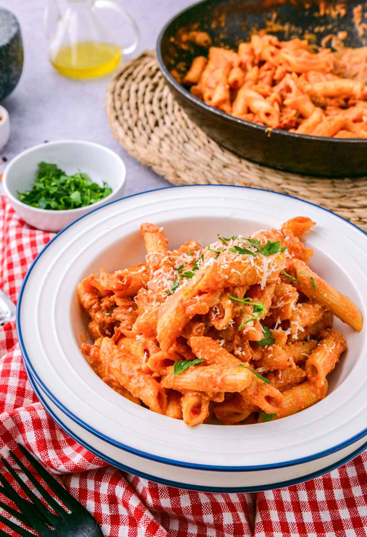 bowl of penne pasta in rose sauce on counter with more behind.