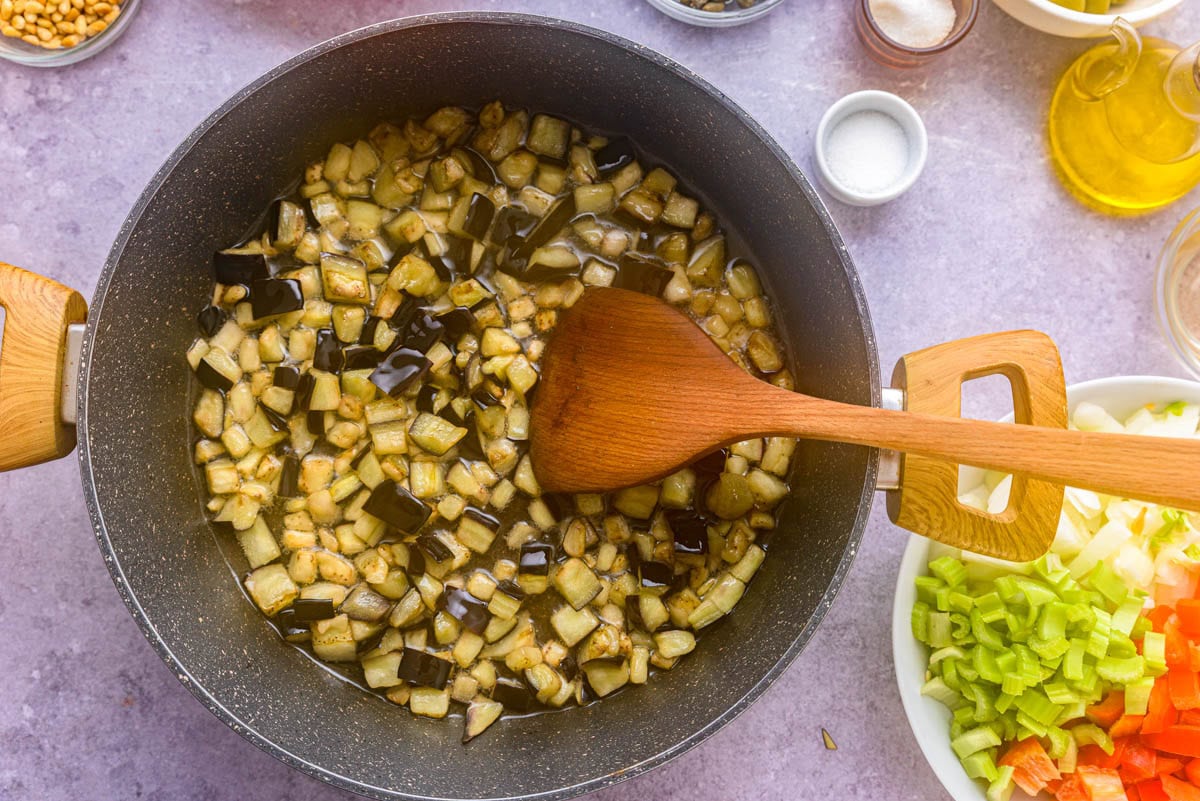 eggplant cooking in black frying pan with ingredients around.