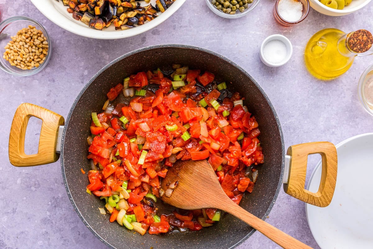 ripe diced tomato added to black frying pan of vegetables.