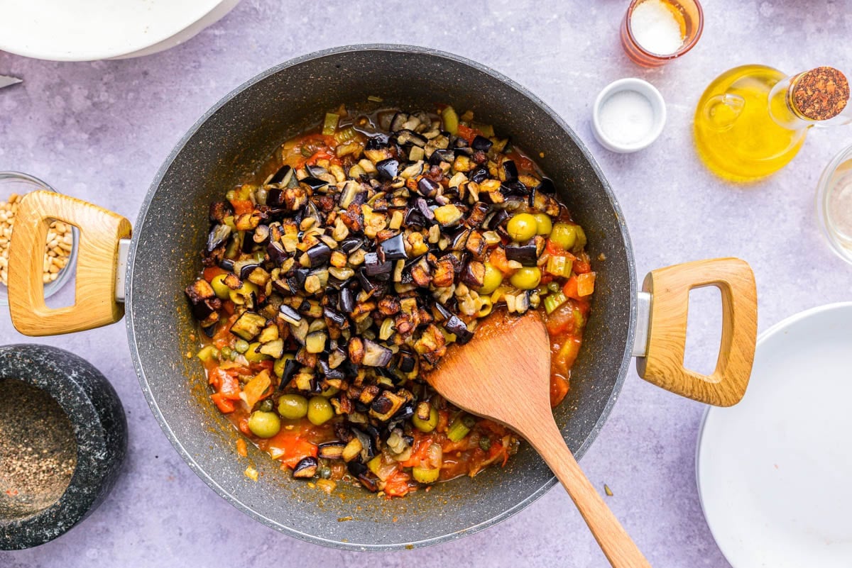 eggplant pieces added back to vegetable stew in black frying pan.