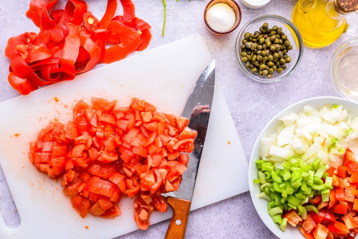 ripe tomatoes chopped on cutting board with knife beside.