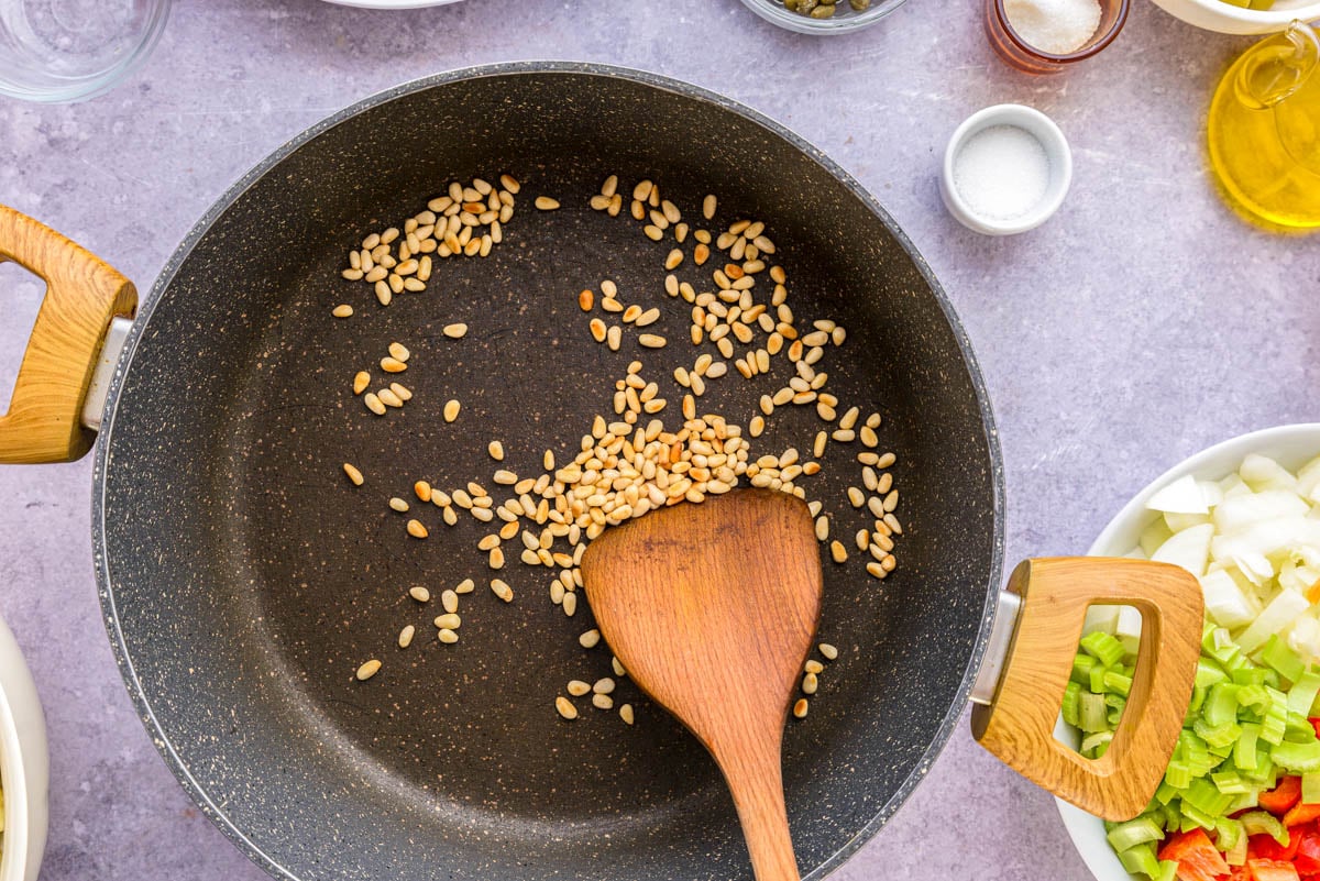 wooden spatula roasting pine nuts in black frying pan.