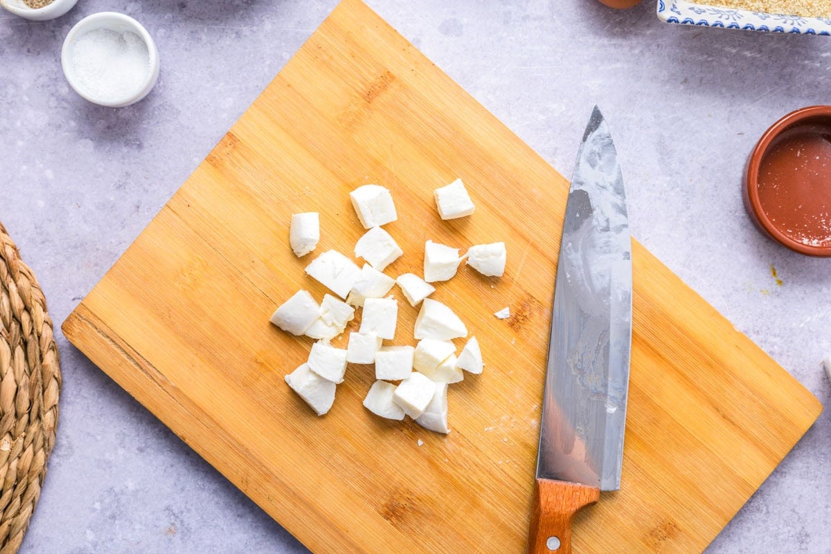 mozzarella ball cut up into pieces on wooden board.