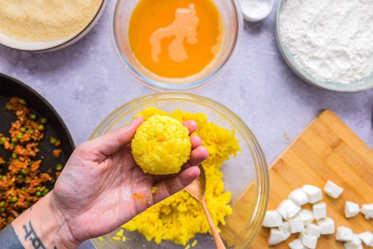 hand holding round ball of yellow rice for arancini ball.