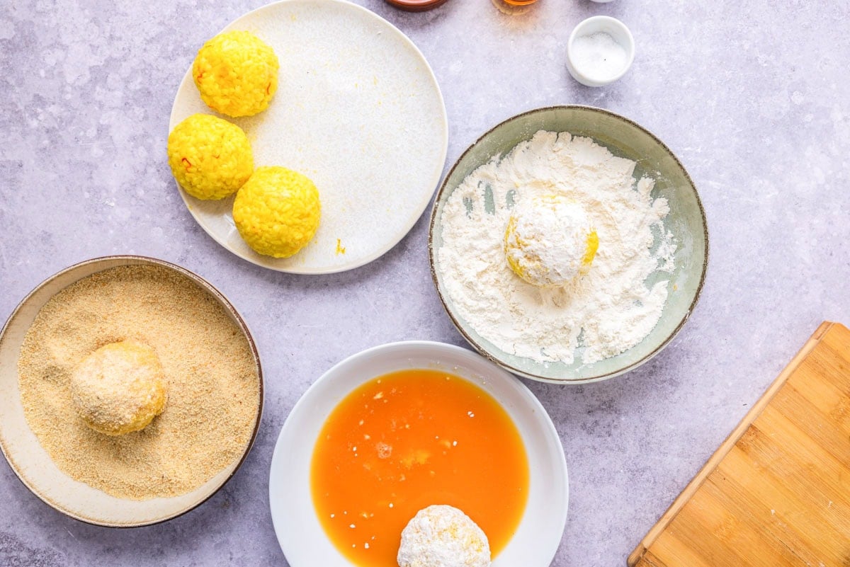 rice balls being passed through breading station on counter.