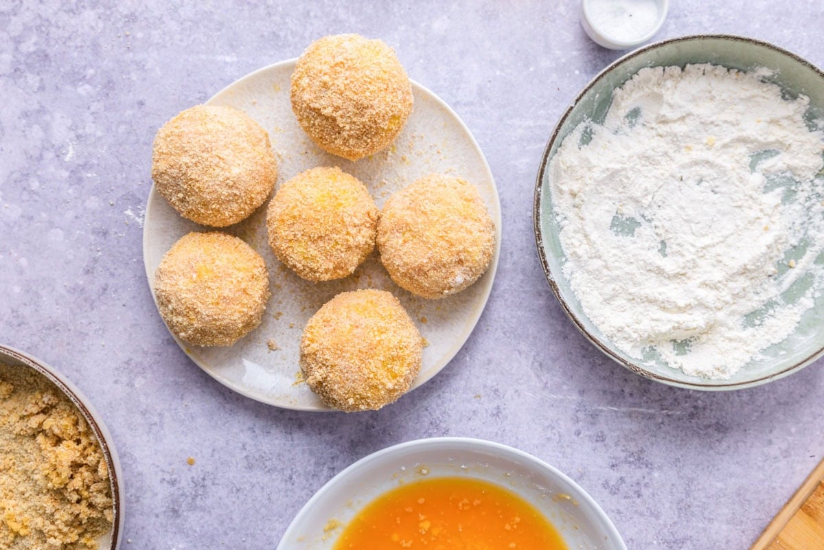 breaded but raw rice balls on plate on counter.