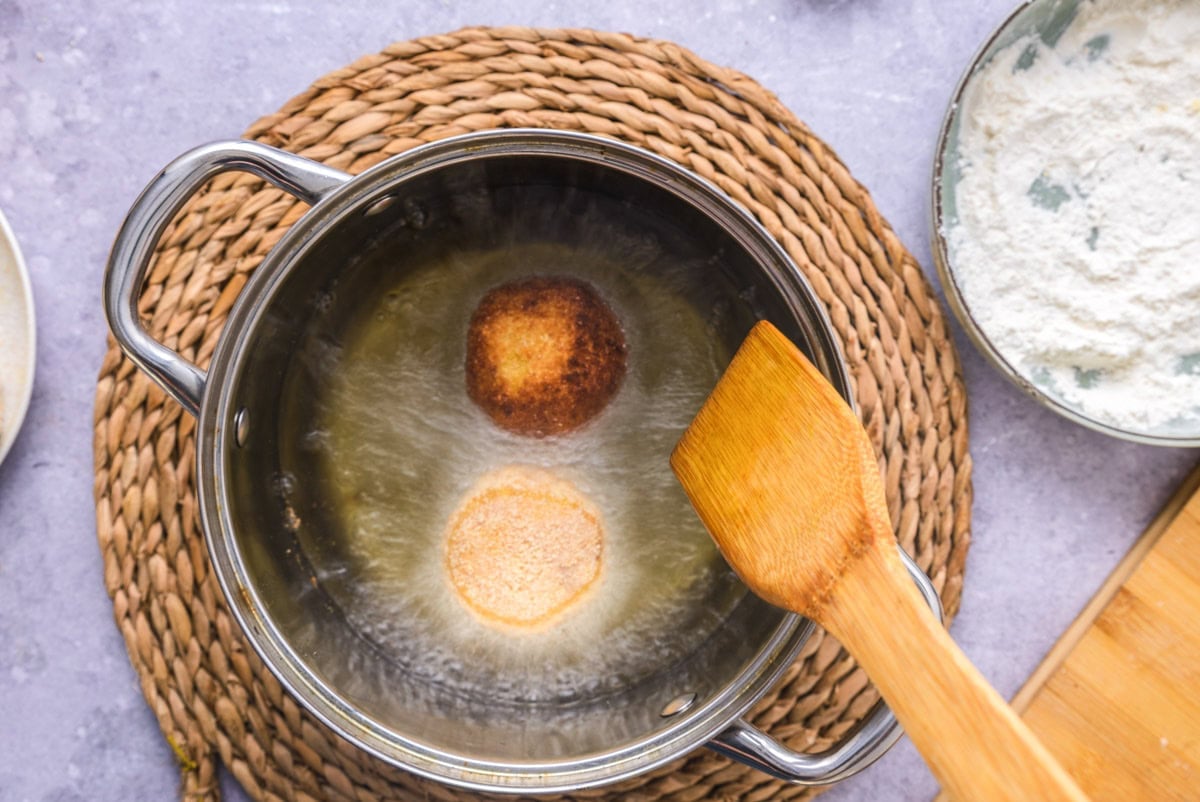 italian rice balls being deep fried in pot of oil.
