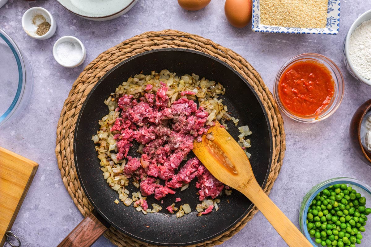 red raw beef in frying pan with browned onions.