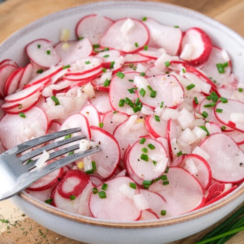 silver fork piercing sliced radish salad in bowl.