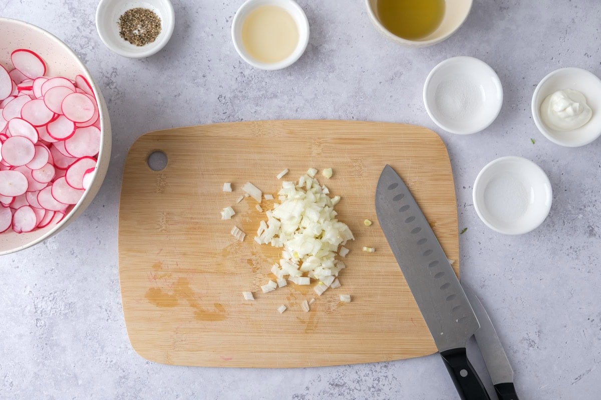 white onion chopped small on wooden board with knife beside.