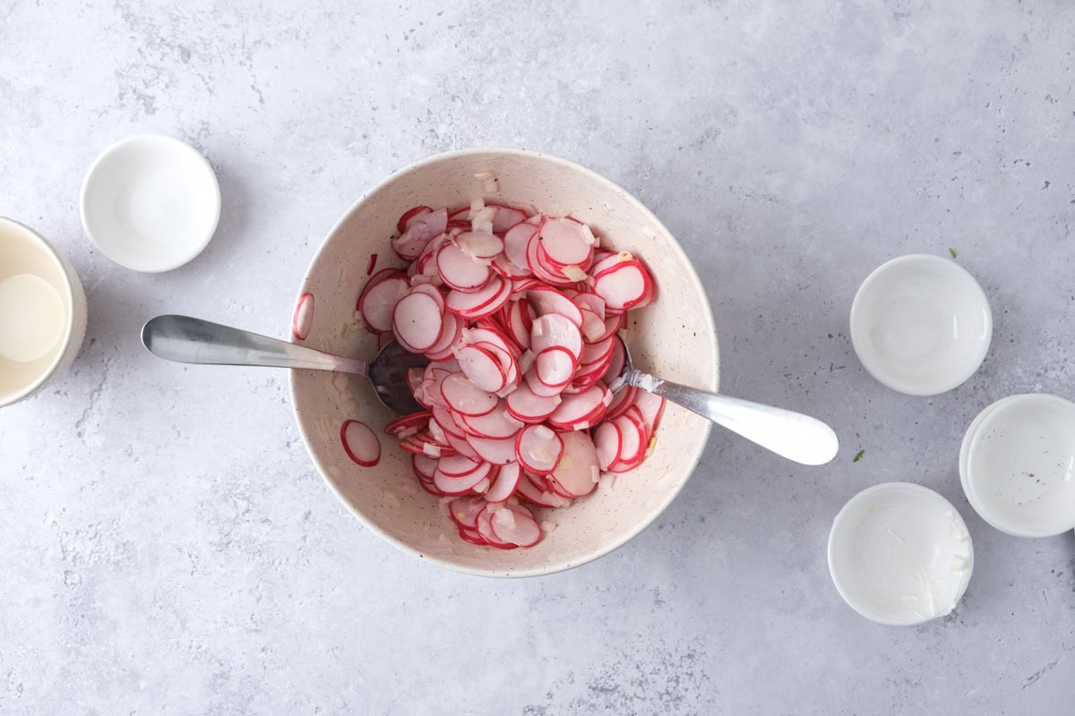 spoons tossing radish salad in bowl on counter.