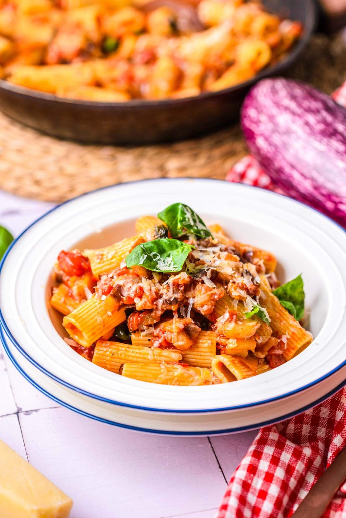 eggplant pasta in a bowl on table with cloth in front.