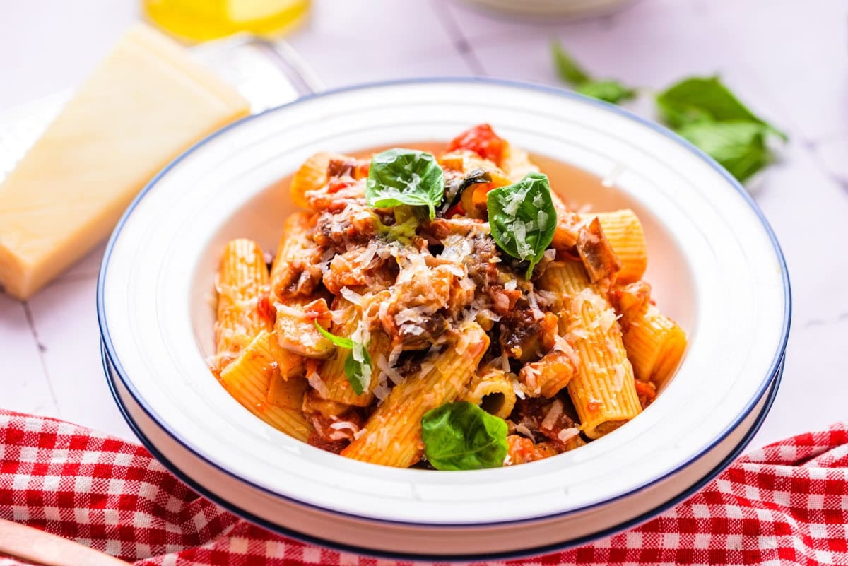 rigatoni pasta in sauce and eggplant pieces in bowl on cloth.
