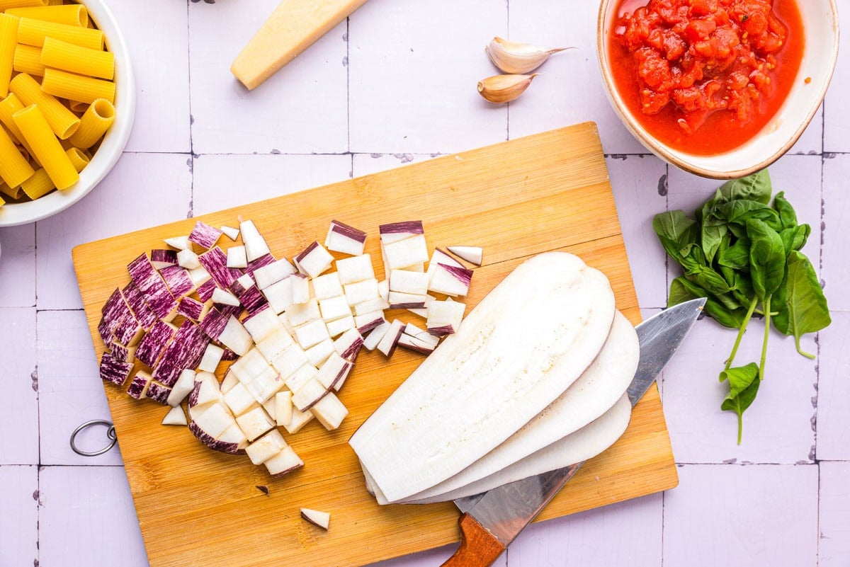 raw eggplant cut into smaller pieces on wooden cutting board.