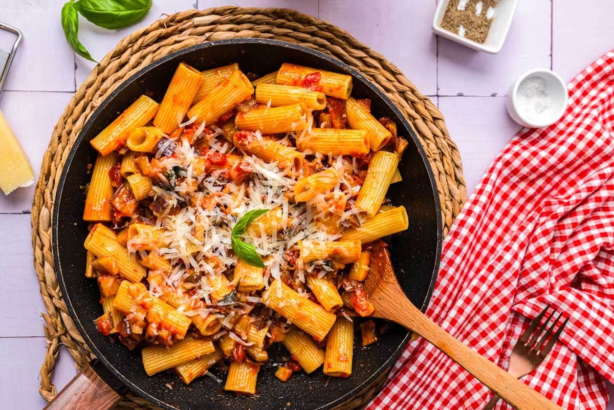 rigatoni pasta with eggplant in pan covered in grated parmesan cheese.