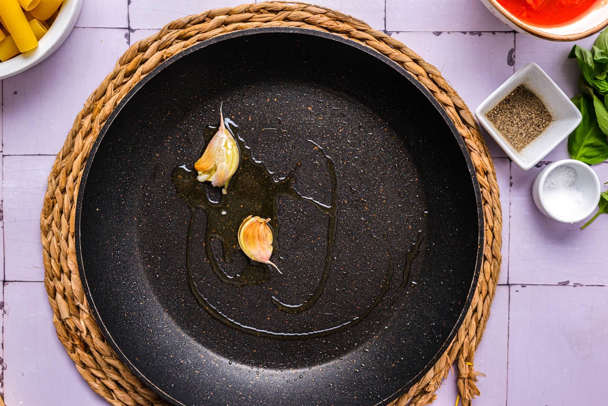 two garlic cloves frying in black pan.