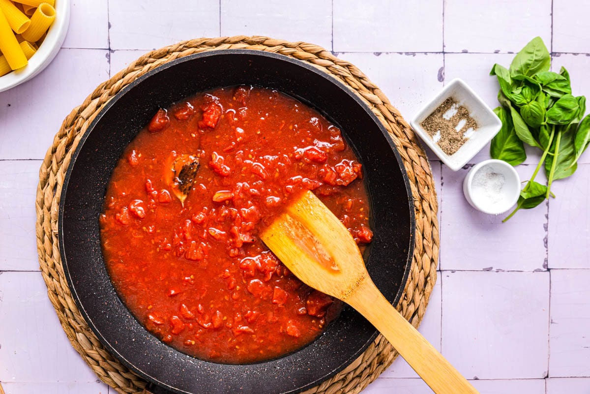 tomato puree being stirred in black pan with wooden spoon.