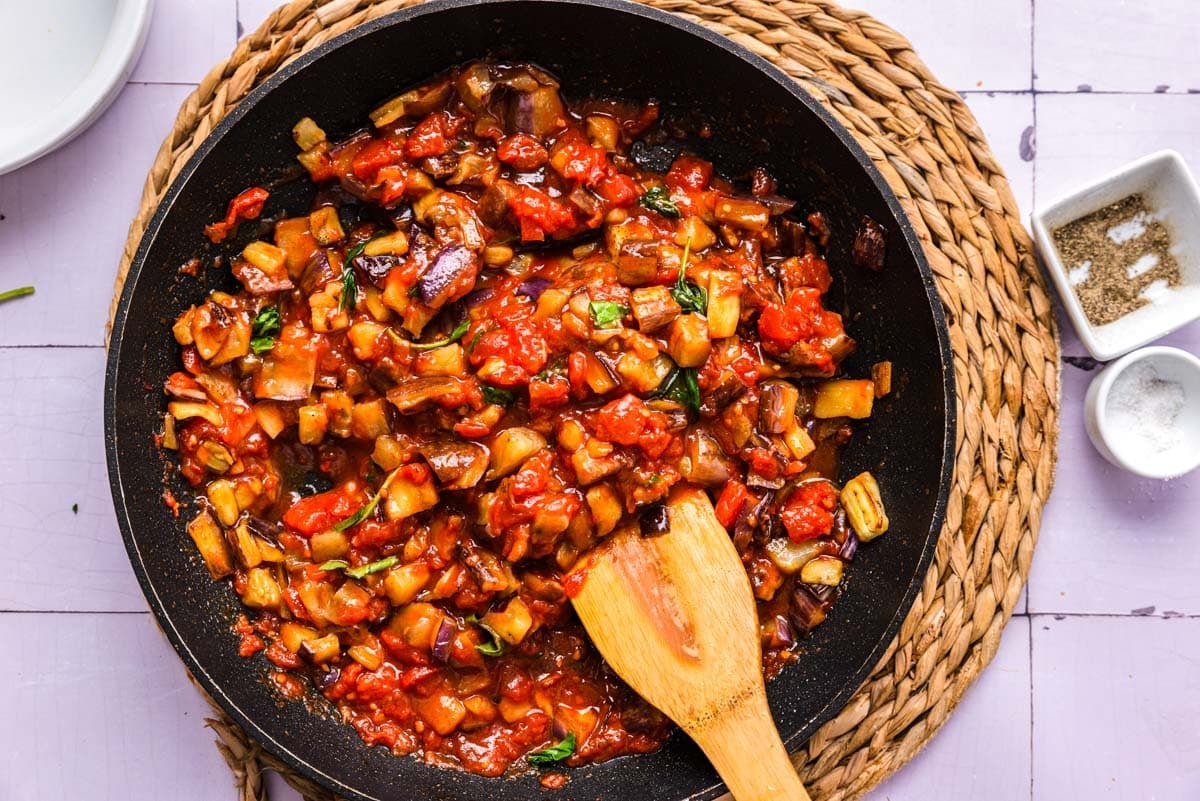 eggplant and basil in red pasta sauce in pan on counter.