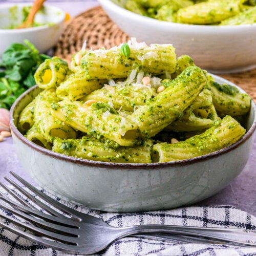 bowl of italian pesto pasta with cloth and forks in front.