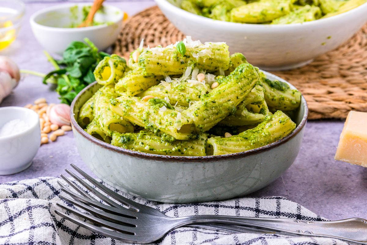 bowl of italian pesto pasta with cloth and forks in front.