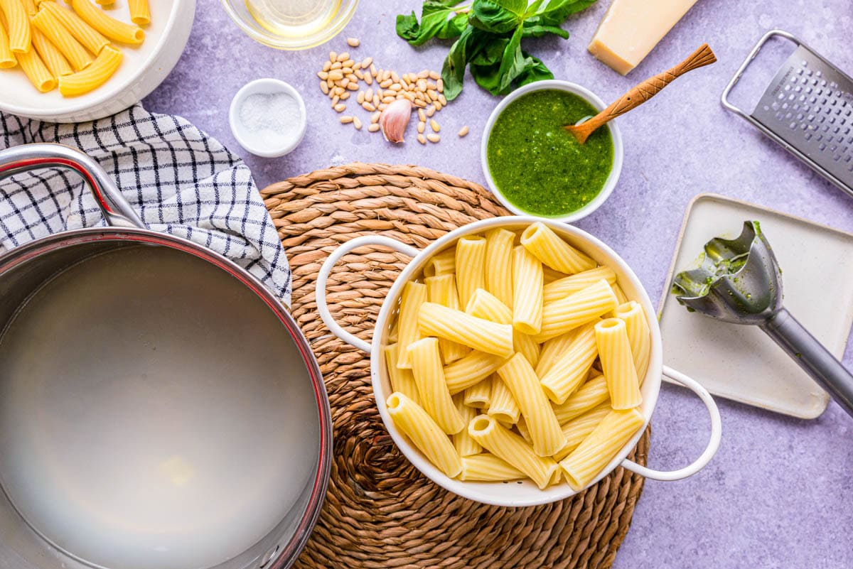 green pesto sauce beside pasta noodles on counter.