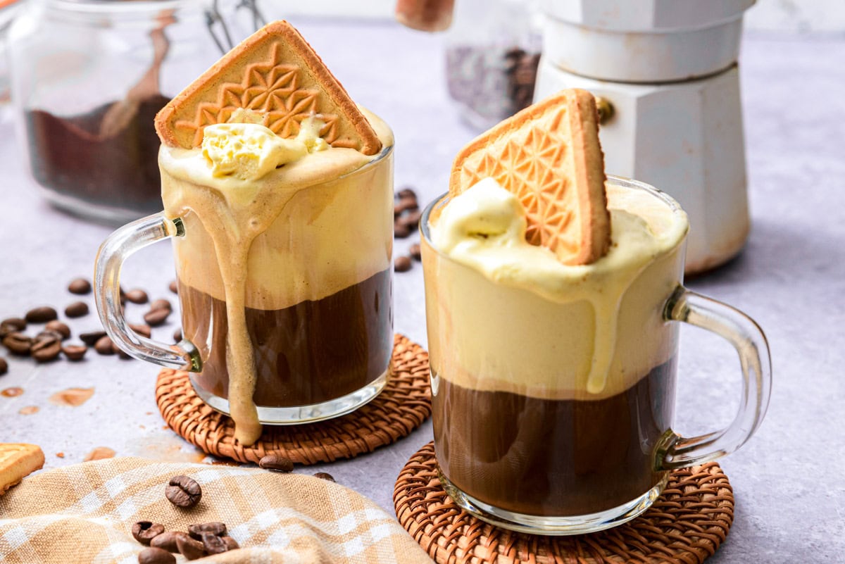 two affogato on cork coasters on counter top with coffee around.