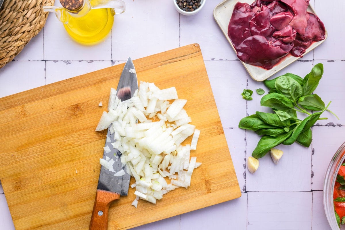 onion diced on wooden board with knife beside.