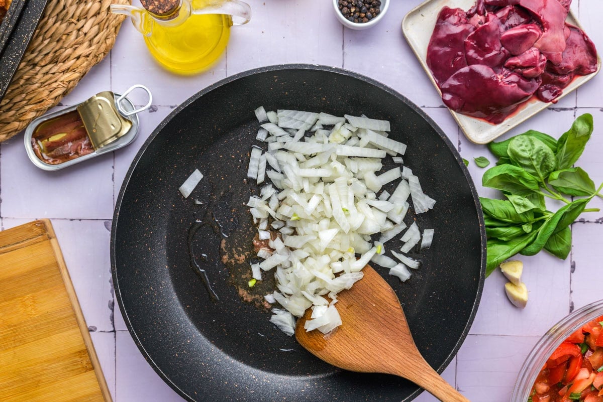 raw diced onions added into black frying pan with anchovies.