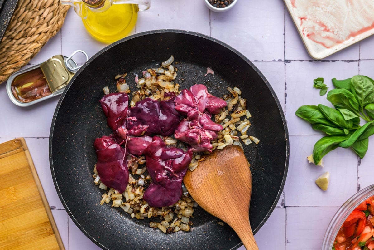raw chicken livers added to cooked onions in frying pan.