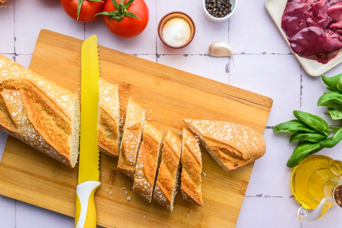crusty bread cut into slices on wooden cutting board with yellow knife.