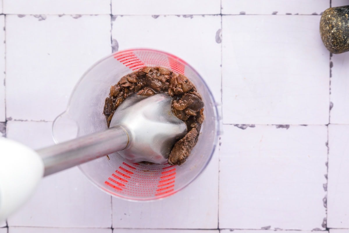 chicken liver being blended by hand blender in blending vessel.