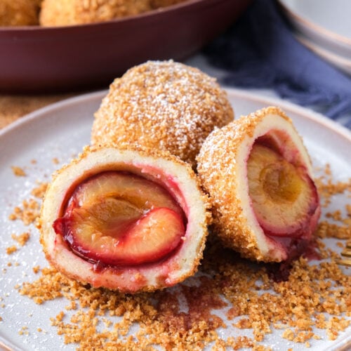 plum dumplings cut open on plate with forks and breadcrumbs around.
