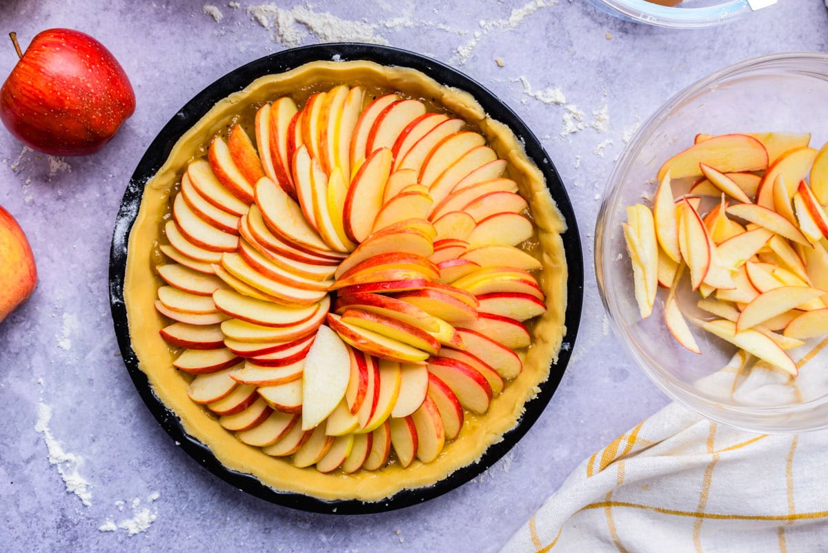 apple slices arranged in circles in raw pie crust on counter.
