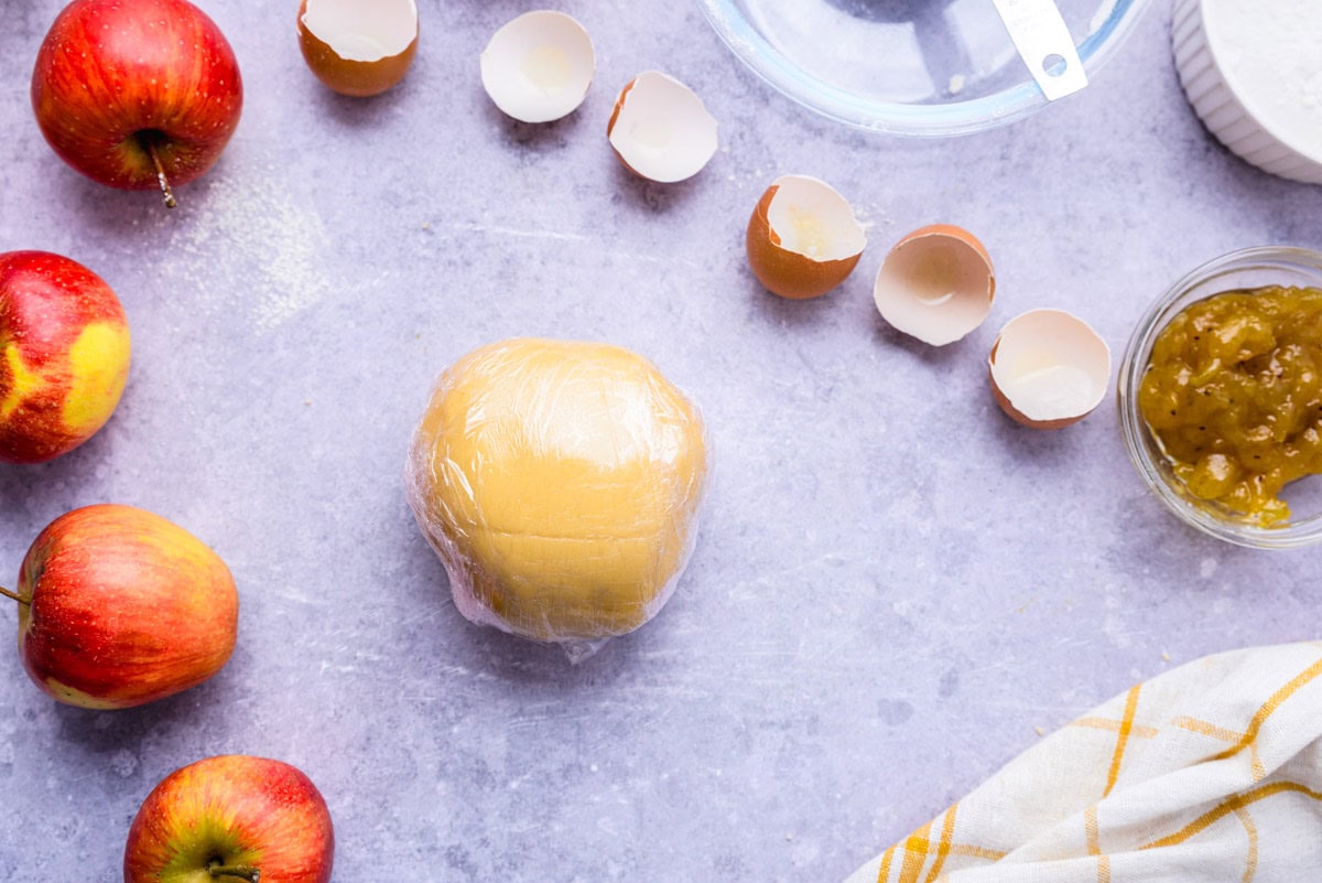 ball of dough wrapped in plastic wrap on counter.