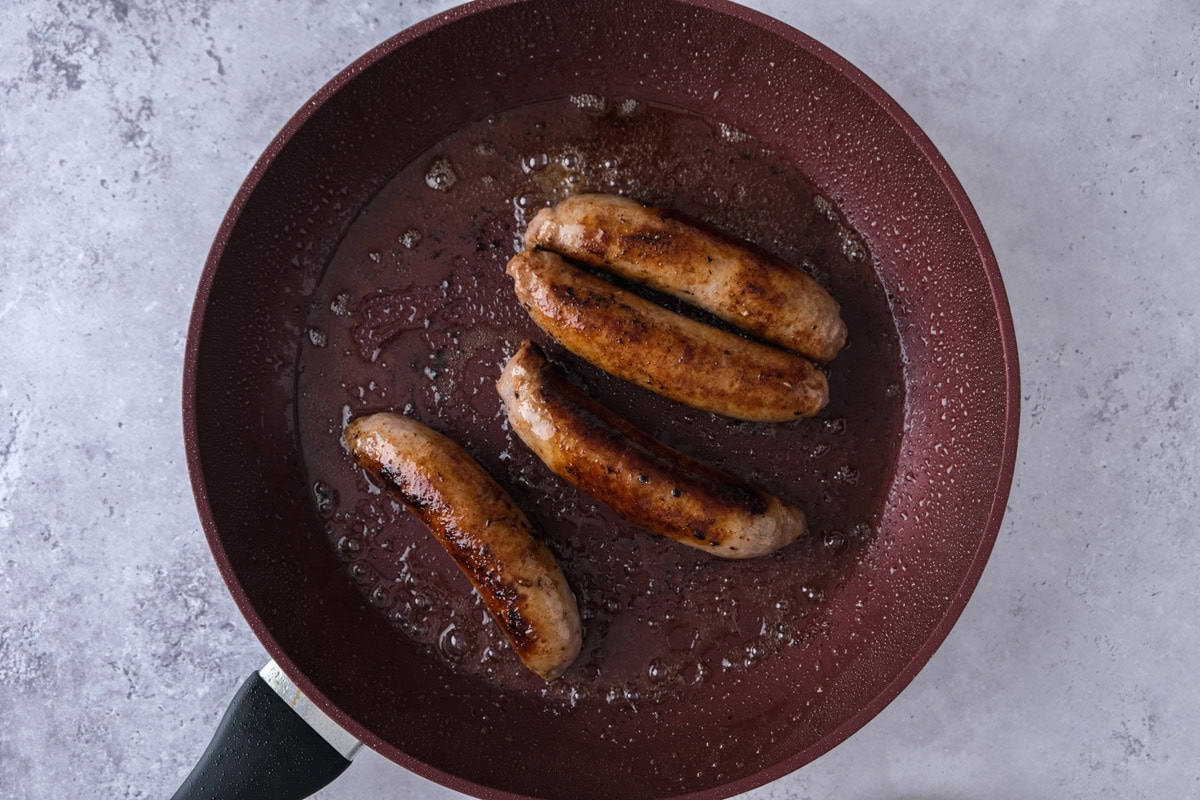 four cooked bratwurst sausages in frying pan.