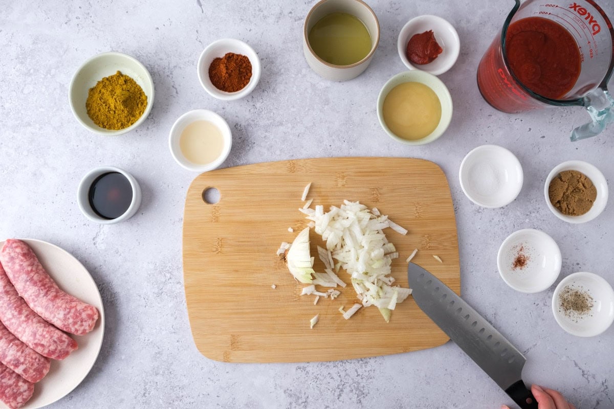 knife cutting onions on wooden board on counter with ingredients around.