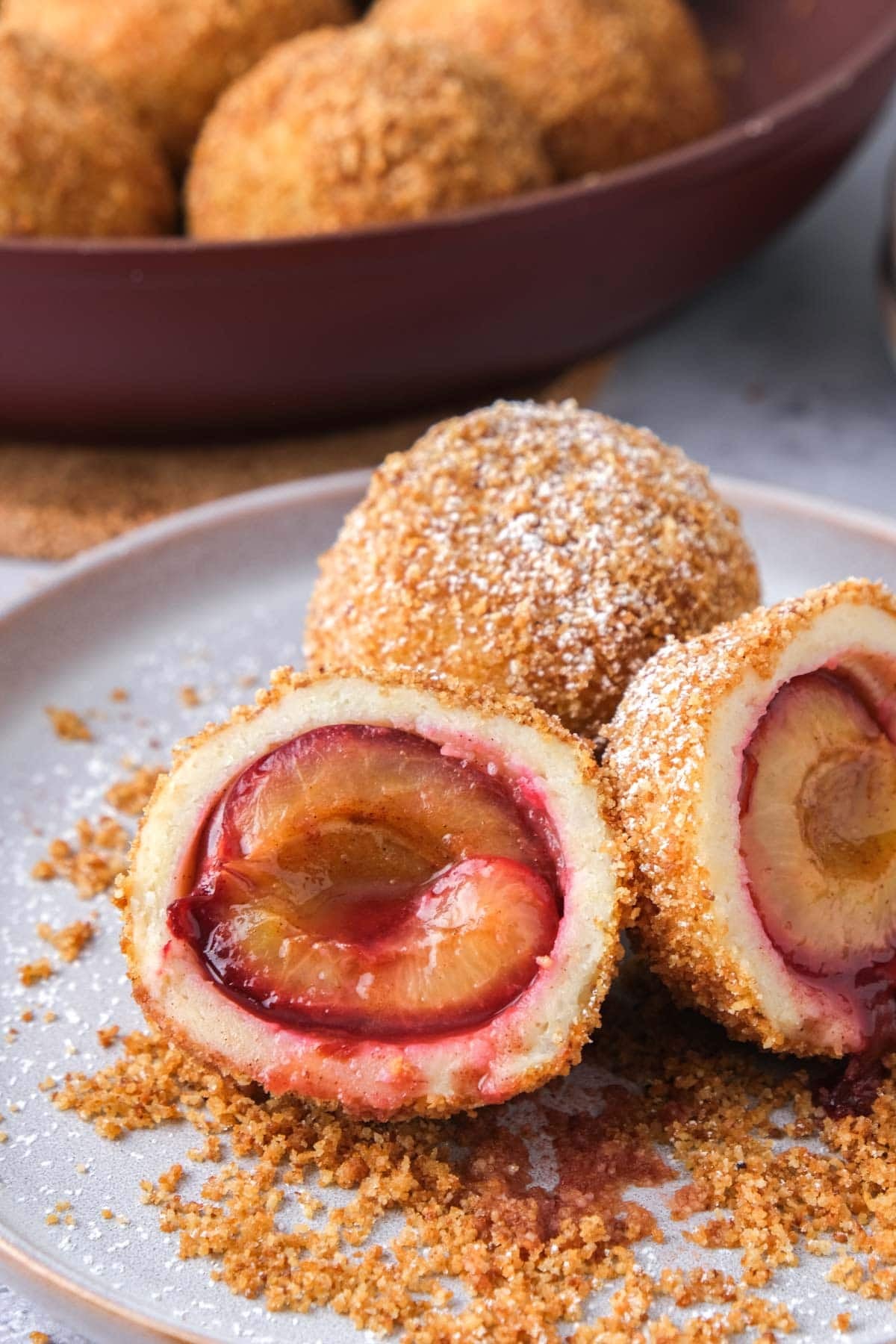 plum dumpling cut in half on plate with breadcrumbs around.