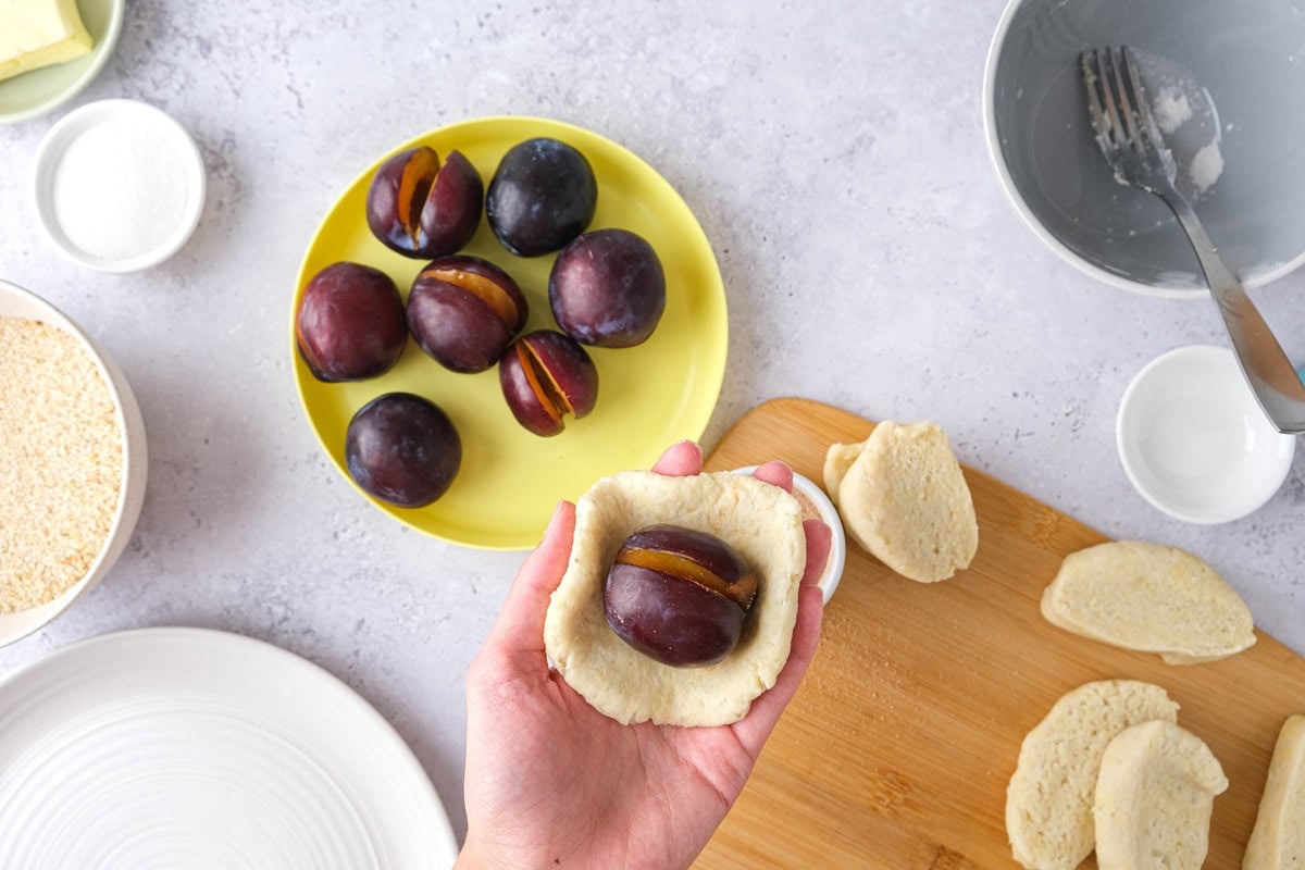hand holding raw plum semi-wrapped in dough.