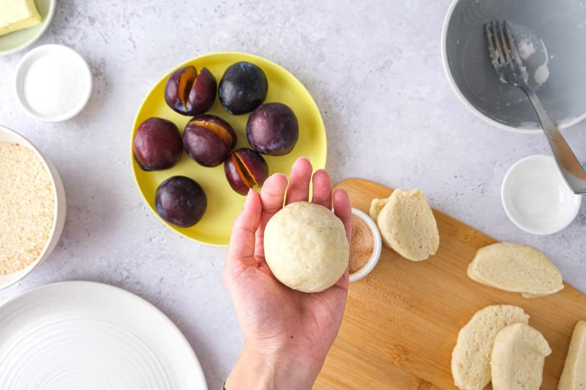 raw plum dumpling held in hand above other ingredients on counter.