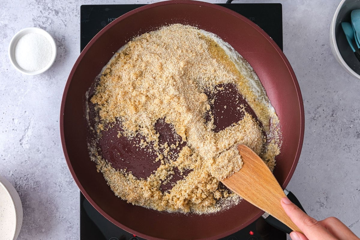 wooden spatula moving butter and breadcrumbs in frying pan.