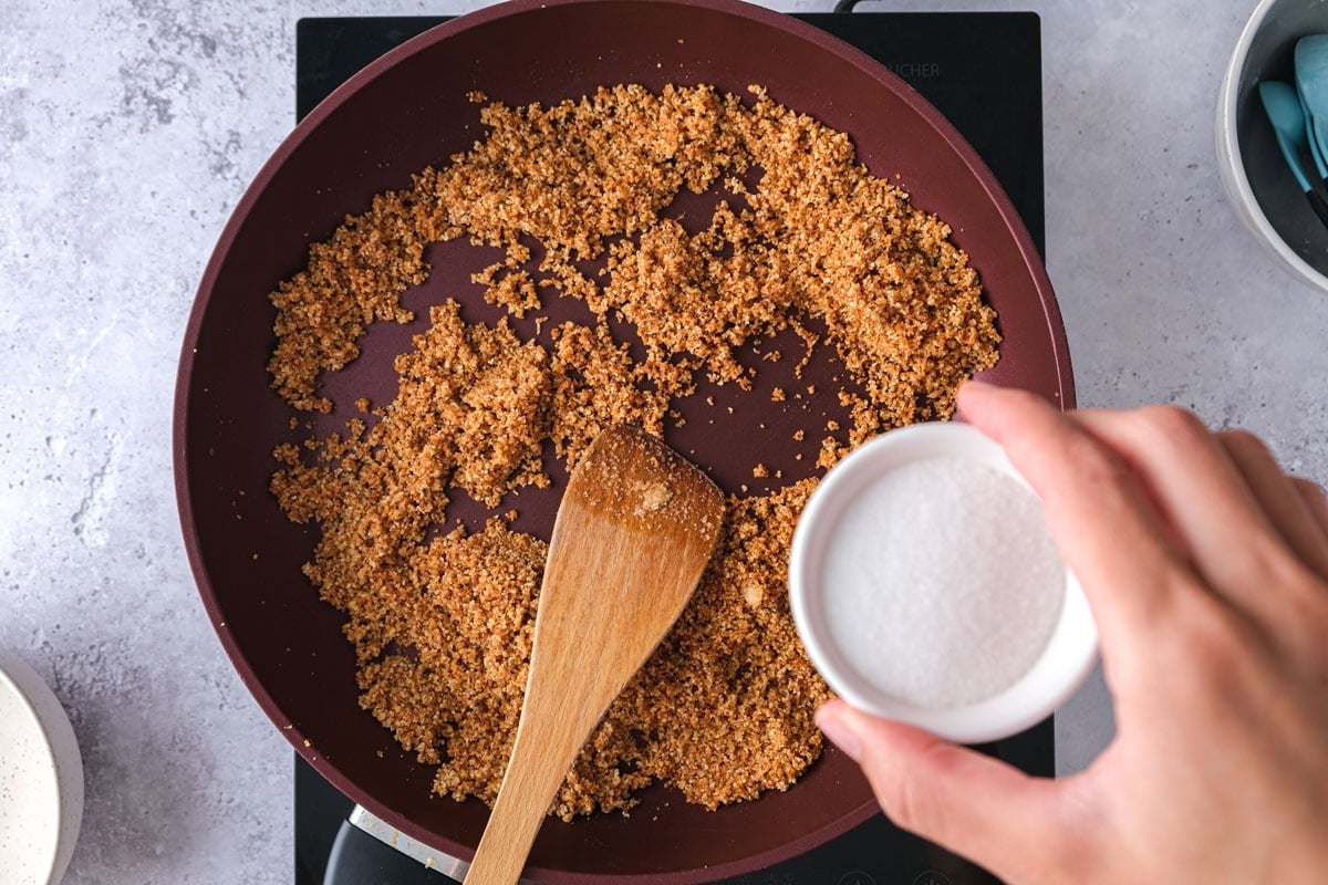toasted breadcrumbs in frying pan with sugar being added to it.