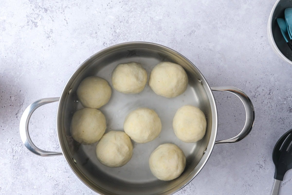 raw plum dumplings in pot of water on counter.