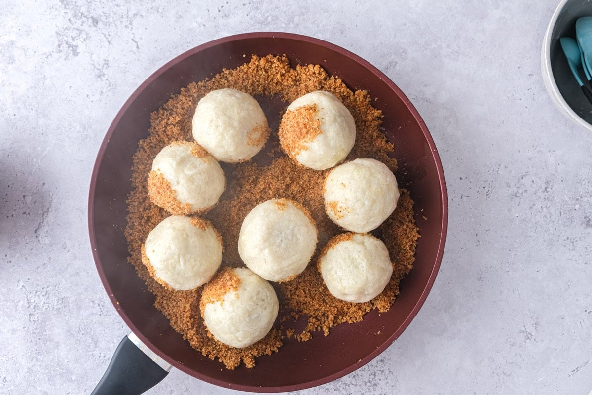 plum dumplings being coated in breadcrumbs in frying pan.